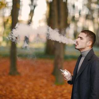 man in the autumn park smoking from an electronic cigarette